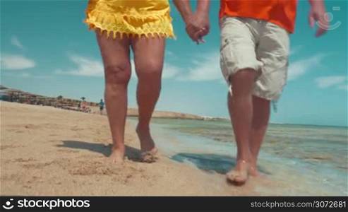 Steadicam shot of mature couple walking by the sea holding hands and talking.