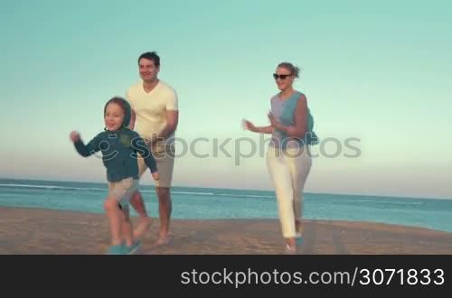 Steadicam shot of mother and fathrer running a race with son on the beach. Boy running up to broken buoy and kicking it, parents applauding to little winner