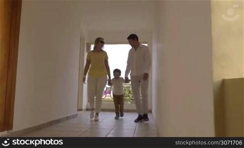 Steadicam shot of mother, father and little son in hotel corridor. Happy naughty boy escaping from parents and running along the hall