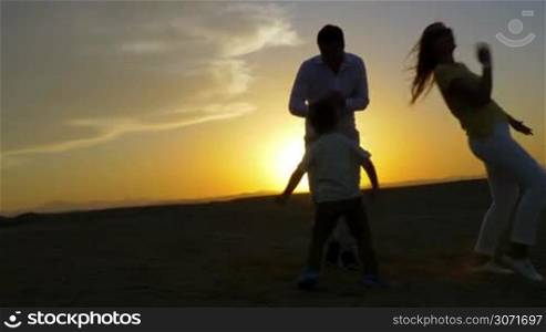 Steadicam shot of parents and son dancing on the beach at sunset.