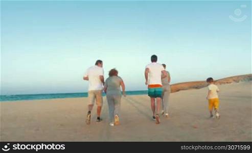 Steadicam shot of parents, child and grandparents jogging in the evening on vacation and reaching sea. Active family holidays