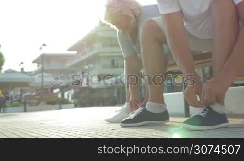 Steadicam shot of senior couple lacing sneakers sitting on the street bench. Ready to start the workout