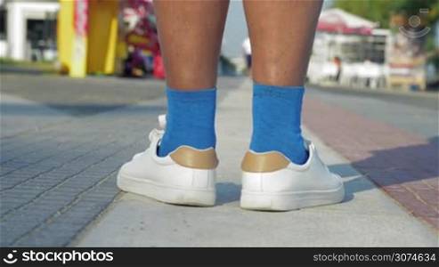 Steadicam shot of senior woman speed walking along the street, view to the feet in blue socks and white trainers