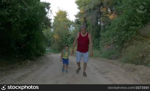 Steadicam shot of tired man and little boy hiking along the country road in sunny day.