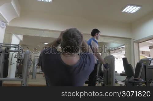 Steadicam shot of two people working out in the gym. One man doing situps on abdominal bench while another one starting chest press after break