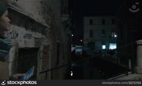 Steadicam shot of woman tourist using tablet PC to make photo of small canal in Venice at night