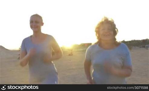 Steadicam shot of young and mature women (or mother and daughter) jogging on the beach in the morning or evening.