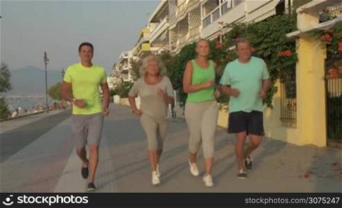Steadicam shot of young and senior couples running along the waterfront in resort town at sunset. Evening jogging to keep fit