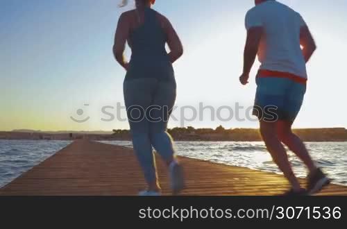 Steadicam shot of young couple ending their morning jogging. They are running turned backs to the camera, then make a jump and deep breath.