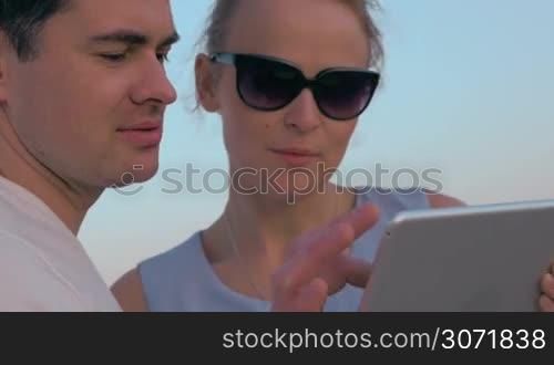 Steadicam shot of young man and woman outdoor with pad. They using tablet computer and enjoying sunset reflecting in womans sunglasses