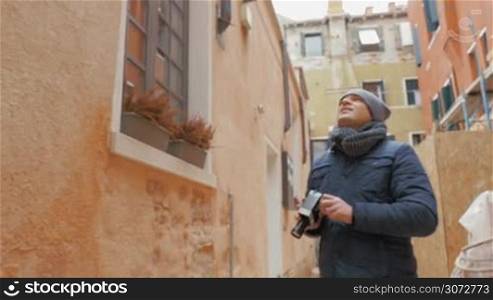 Steadicam shot of young man with vintage handheld camera capturing on video buildings of old city.