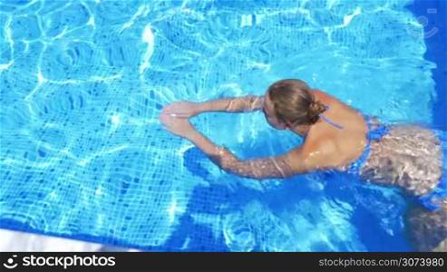 Steadicam shot of young woman swimming in open-air swimming pool in sunny day.