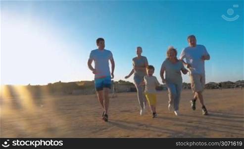 Steadicam slow motion shot of a large family jogging in morning. Little boy is running ahead, his parents and grandparents are following him.