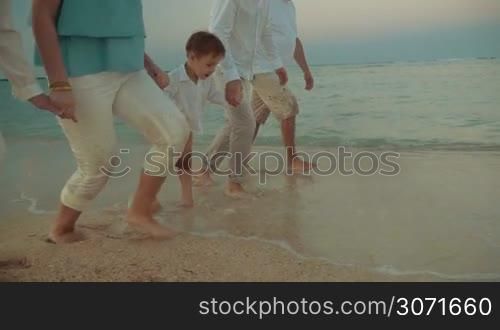 Steadicam slow motion shot of a little boy and his family holding hands and marching in the incoming sea waves. Then the boy begins running and his relatives applause him.
