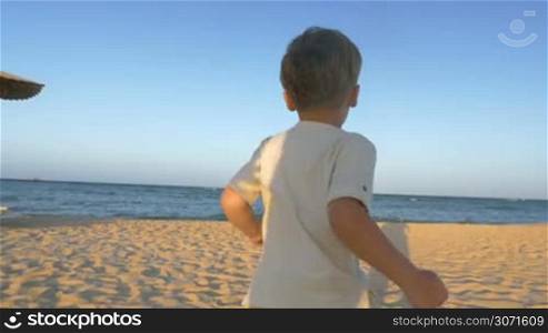 Steadicam slow motion shot of a little boy running to the sea. He is turned his back to the camera.