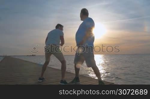 Steadicam slow motion shot of a mature man and his adult son fighting in joke, son is trying to punch father&acute;s palm.