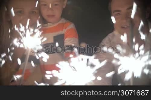 Steadicam slow motion shot of family members lighting Bengal fires. Parents and grandparents of a little boy hunker down around him.