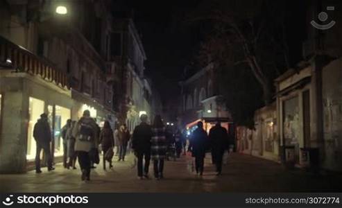 Steadicam slow motion shot of one of the streets in Venice, Italy in spring or fall. People are walking by brightly lit show windows of shops.