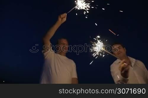 Steadicam slow motion shot of two couples, young and mature, lighting sparklers at night.