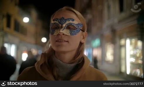 Steadicam slow motion shot of young blonde woman in fancy carnival mask walking in Venice, Italy.