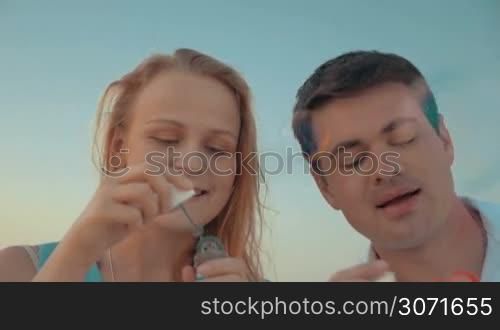 Steadicam slow motion shot of young couple blowing soap bubbles. They are standing on the beach close to each other.