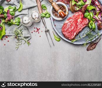 Steak and green salad. Meat preparation and marinating for grill or BBQ on gray stone background, top view, border