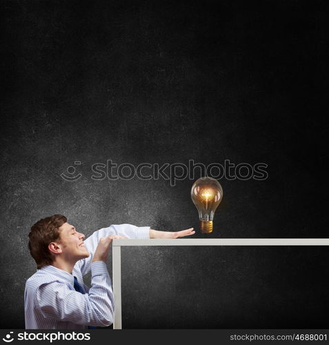 Steal the idea. Young man looking from under table at glass light bulb