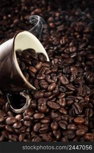 Steam rises over roasted coffee beans, coffee mug lies on fragrant coffee, selective focus on beans, vertical frame