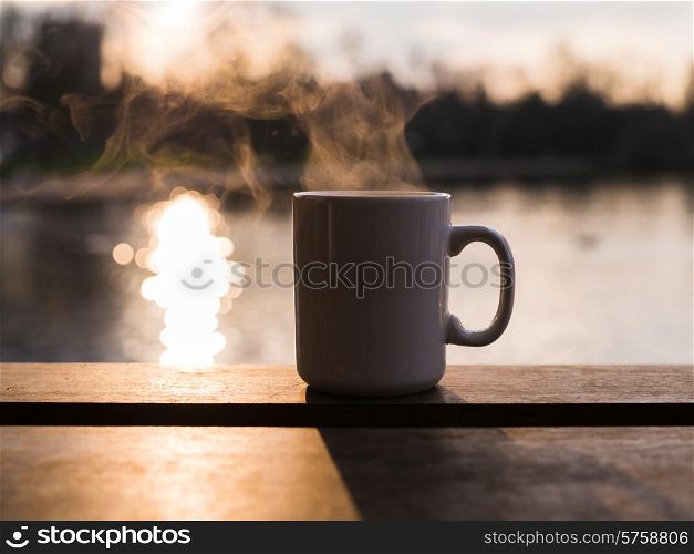 Steam rising from a mug with a hot beverage by a pond at sunset in the winter