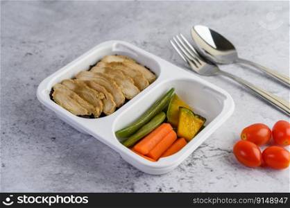 Steamed chicken breast in a plastic box with pumpkin, carrots, long-hatched beans and tomato. Selective focus.