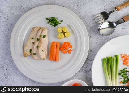 Steamed chicken breast on a white plate with spring onions and chopped carrots. Selective focus.