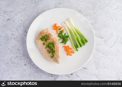 Steamed chicken breast on a white plate with spring onions and chopped carrots. Selective focus.