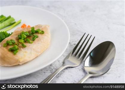 Steamed chicken breast on a white plate with spring onions and chopped carrots. Selective focus.