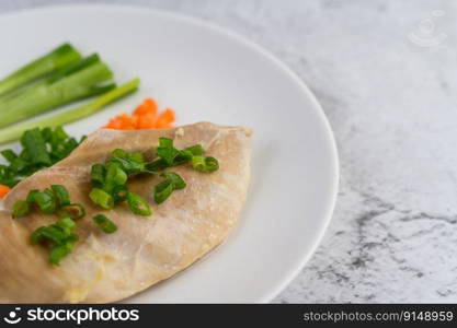 Steamed chicken breast on a white plate with spring onions and chopped carrots. Selective focus.