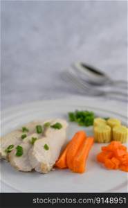 Steamed chicken breast on a white plate with spring onions, baby corn, and chopped carrots. Selective focus.