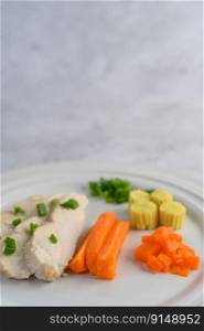 Steamed chicken breast on a white plate with spring onions, baby corn, and chopped carrots. Selective focus.