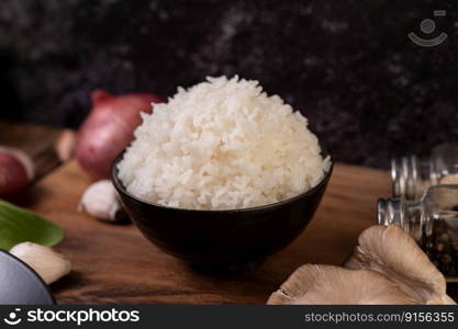 Steamed rice in a bowl with garlic and red onion on a wooden cutting board.