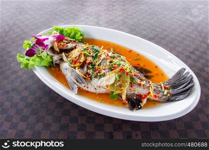 Steamed sea bass fish with lemon put a white ceramic dish on leather floor the grid pattern.