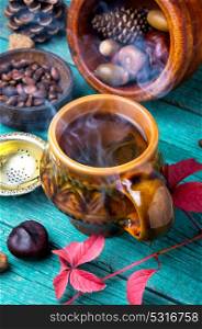 steaming cup of autumn tea. Cup with hot autumnal tea, on background of autumn foliage, cones and nuts