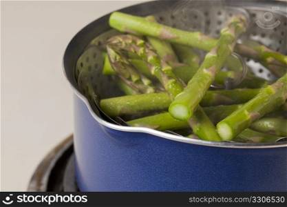 steaming green asparagus in a steamer basket inside blue pot