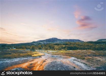 Steamy river with a geyser basin in a beautiful landscape with mountains in the background