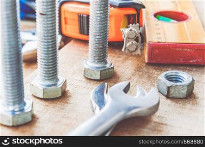 Steel bolt nuts and washers lie on wooden boards near an adjustable spanner and a tape measure. The concept of tools and repair work.. Steel bolt nuts and washers lie on wooden boards near an adjustable spanner and a tape measure.