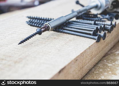 Steel screws lie on a wooden board near the screwdriver. The concept of tools and repair work. Steel screws. Metal screw. Steel screws lie on a wooden board near the screwdriver. The concept of tools and repair work. Steel screws.