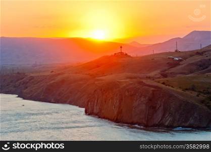 Steep cliff at the edge of the sea at sunset, on the background of the Crimean mountains