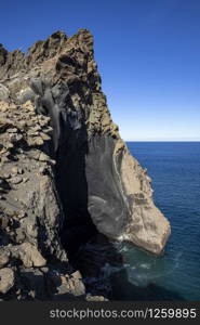 Steep rock edge of brown volcanic crater falls deep into beautiful dark blue water of Antarctica