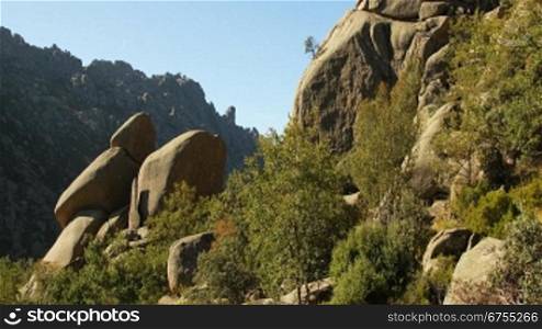 Steingebilde aus wei?en kantigen Steinen in einer grnnen Wiese mit Bnschen, dazwischen Felsen / Steine auf einem Berg; im Hintergrund Berglandschaft.