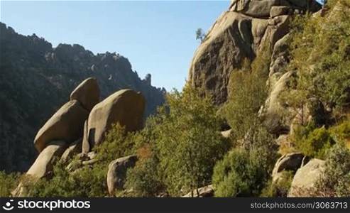 Steingebilde aus wei?en kantigen Steinen in einer grunen Wiese mit Buschen, dazwischen Felsen / Steine auf einem Berg; im Hintergrund Berglandschaft.