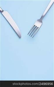 Stell new clean knife and fork on blue pastel paper background, creative flat lay with copy space
