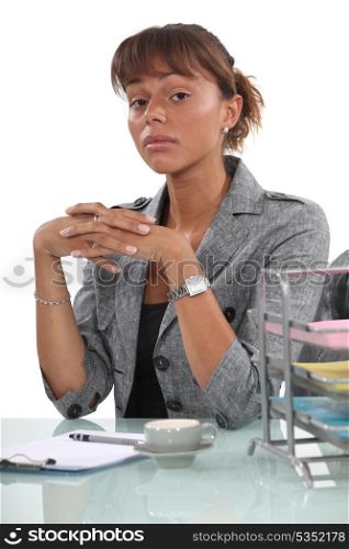 Stern businesswoman with coffee sat at desk