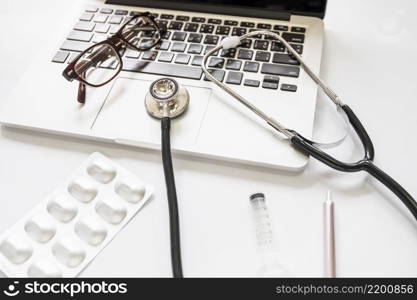 stethoscope eyeglasses laptop keypad with medicine pack syringe pen white background